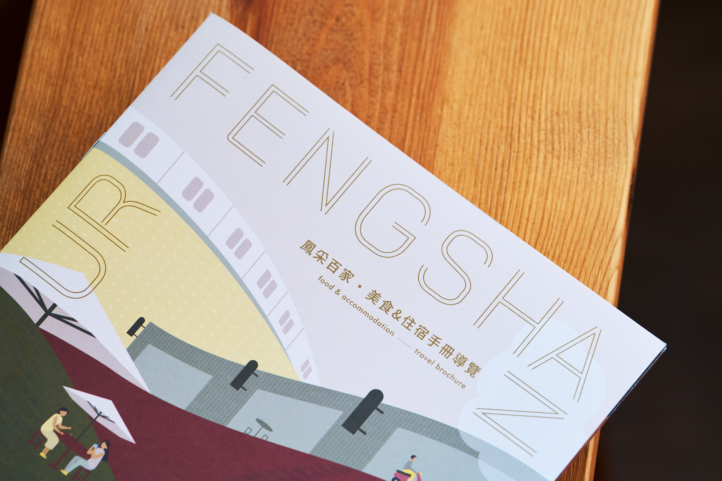 鳳采百家導覽手冊封面上緣與插畫置於木桌的近拍