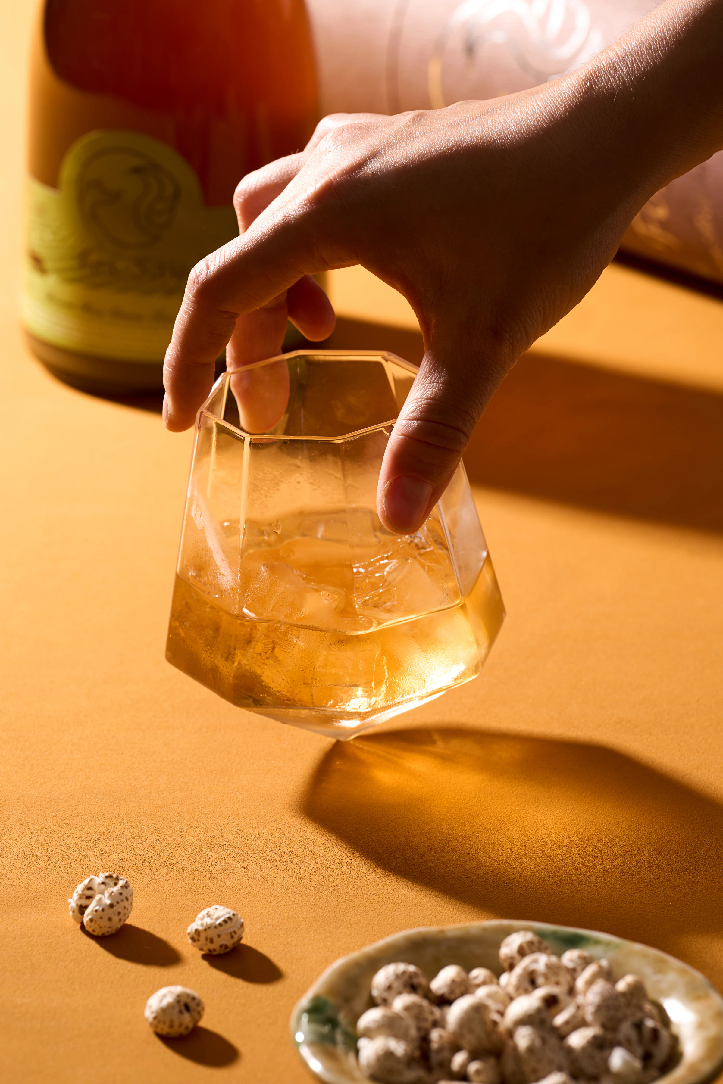 狐說茶酒暖黃桌面上手持冰塊杯的直式情境攝影