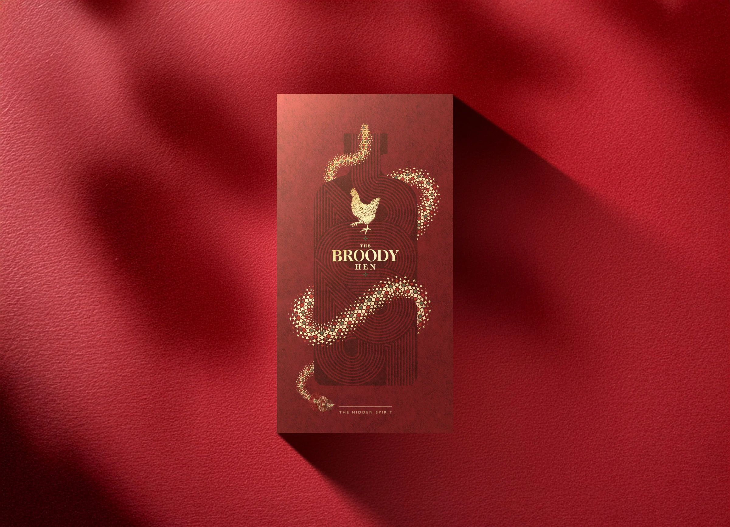 The Broody Hen 紅金禮盒正面，呈現母雞標誌、蛇形花紋與酒瓶輪廓